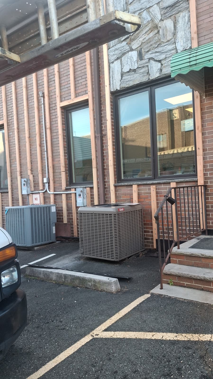Vertical pressure-treated 2x4 furring nailed over existing brick façade, carefully routed around HVAC condensers, conduit and electrical boxes